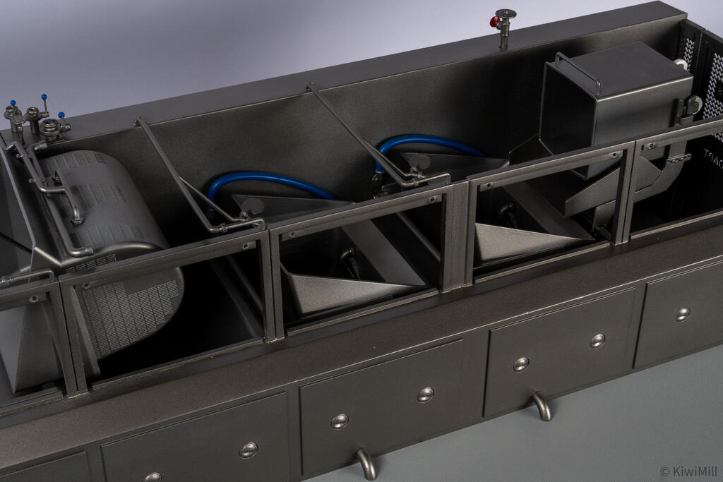 Close-up of the cooking line interior: perforated cooking basket, angled chutes, blue hoses and drain spouts